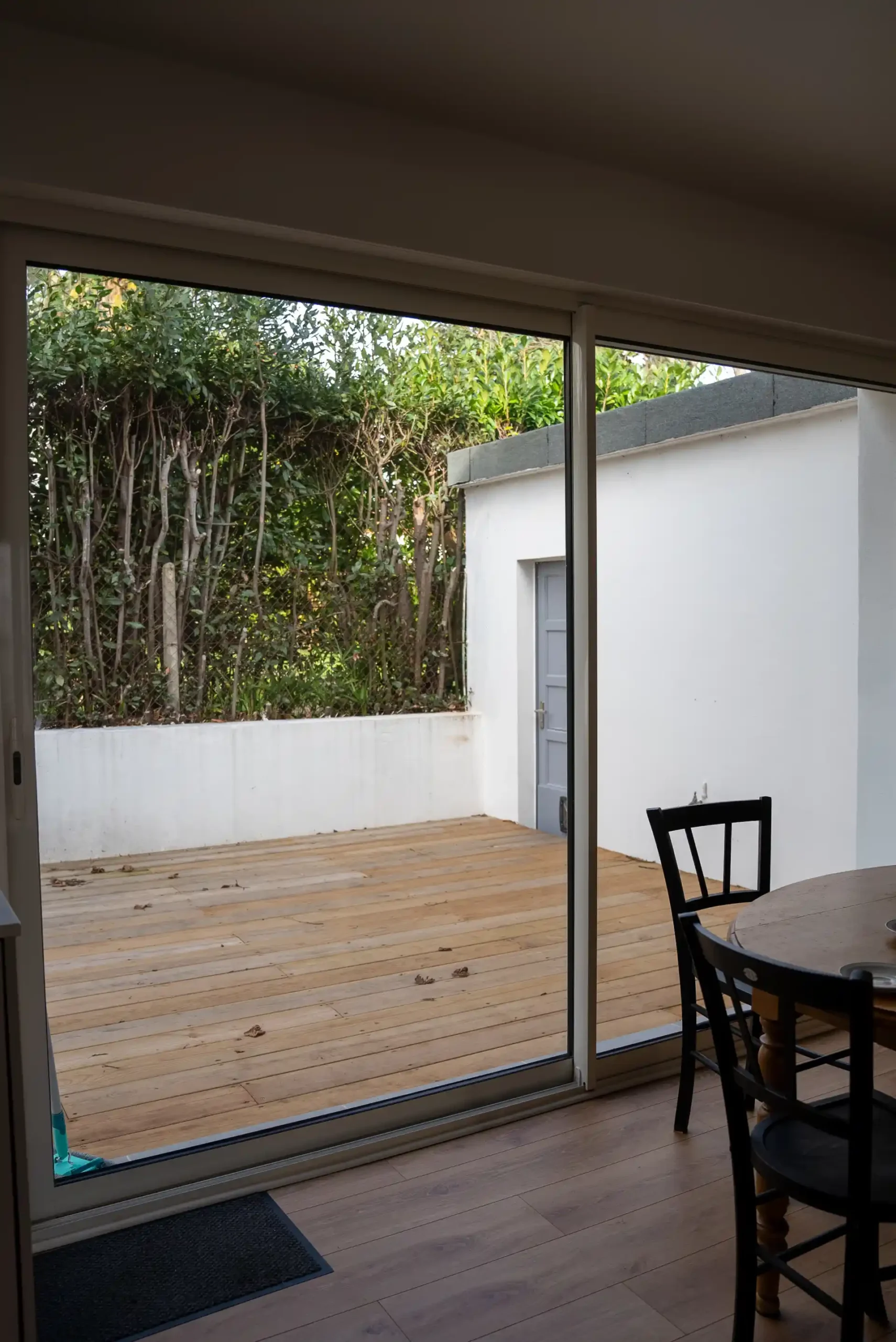 Baie vitrée coulissante en aluminium ouverte sur une terrasse en bois depuis un séjour rénové