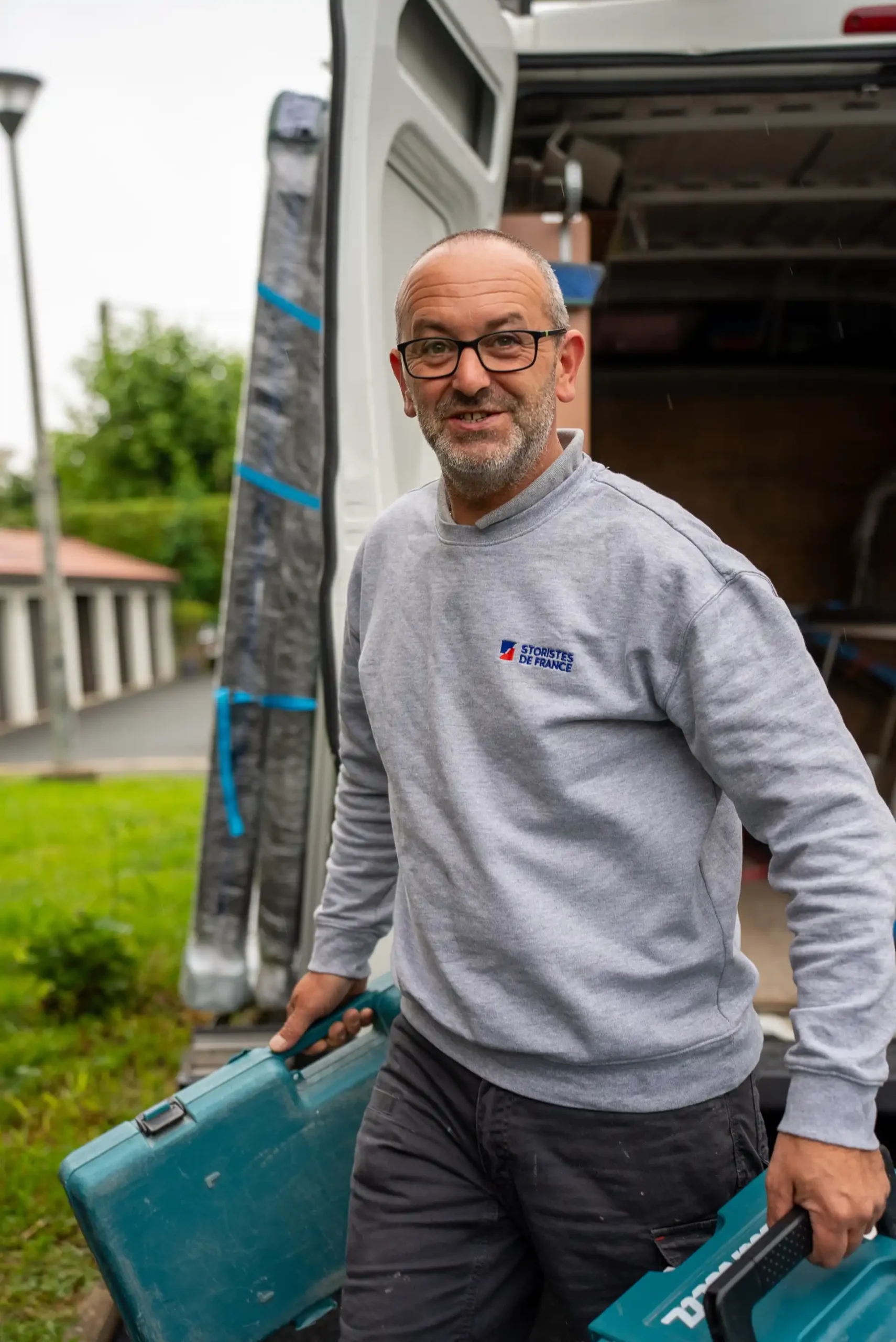 Artisan Storistes de France souriant devant son camion avec deux caisses à outils Makita avant une intervention