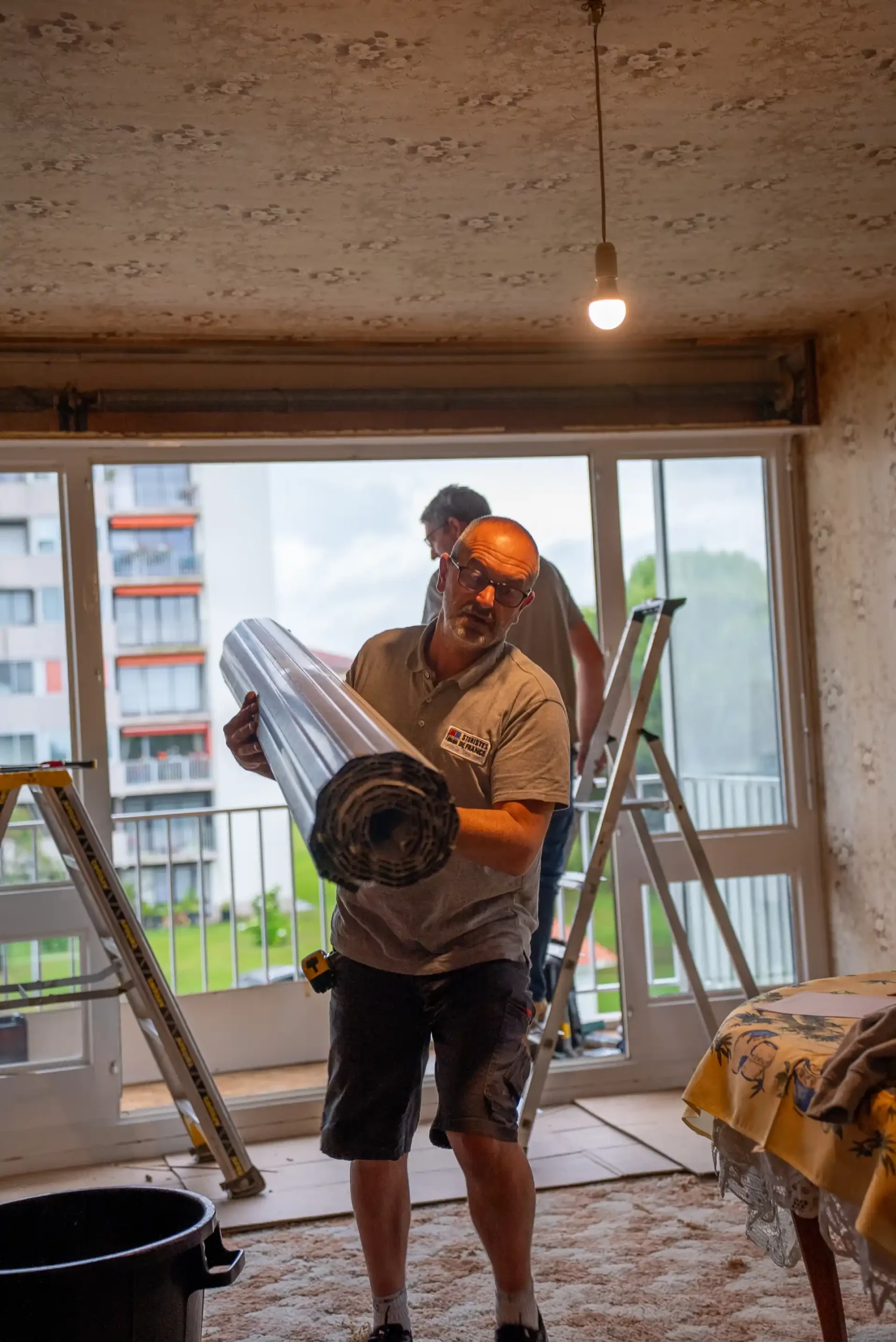 Artisan portant un tablier de volet roulant aluminium pour remplacement dans un appartement