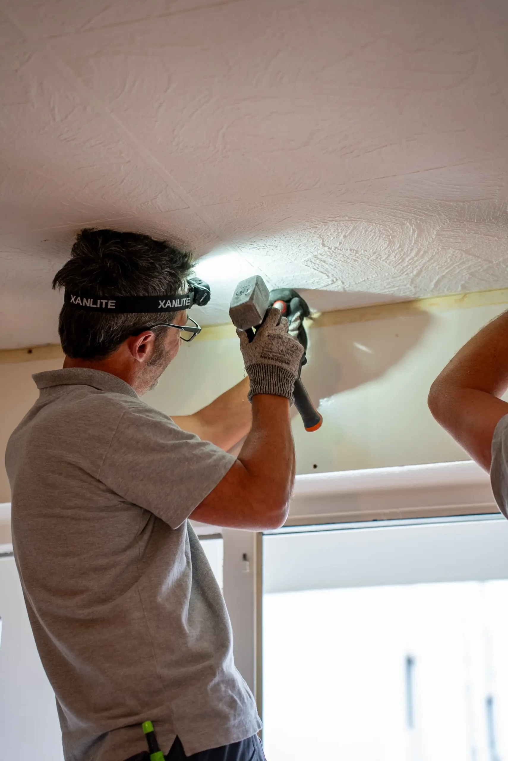Artisan fixant le coffre d'un volet roulant aluminium au marteau dans un chantier de rénovation